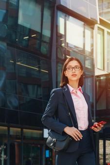 オフィスビルの外でスマートフォンを持って立つビジネスウーマン ビジネスウーマン,ビジネス,女性の写真素材