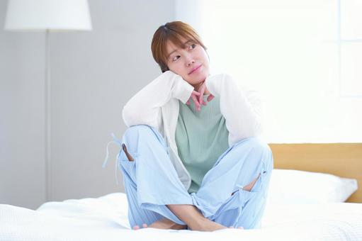ベッドに座り横を見ている女性 女性,見る,頬杖の写真素材