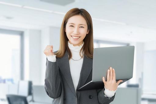 パソコンを持ってガッツポーズをする女性 女性,ガッツポーズ,笑顔の写真素材