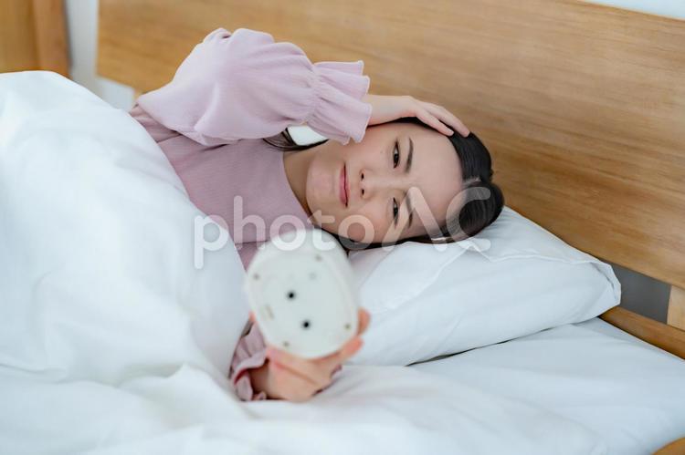 目覚まし時計を見る女性 不眠,寝坊,鬱の写真素材