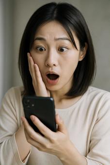 スマホを見て驚く女性 スマホを見て驚く女性の写真