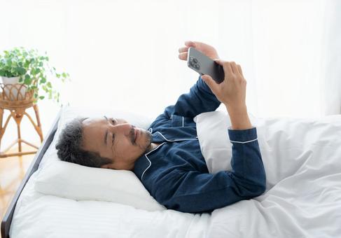 寝室でスマホを見るミドルの男性 寝室でスマホを見るミドルの男性 男性,スマホ,ミドルの写真素材