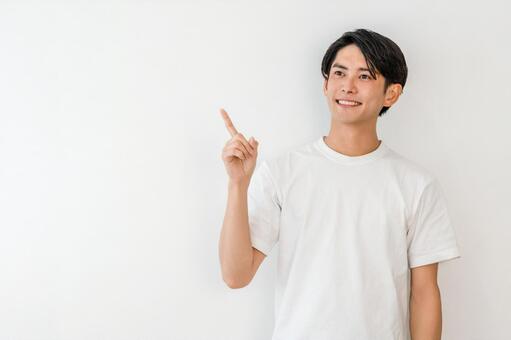 指差しするTシャツ姿の若いアジア人男性 ポイント,紹介,案内の写真素材