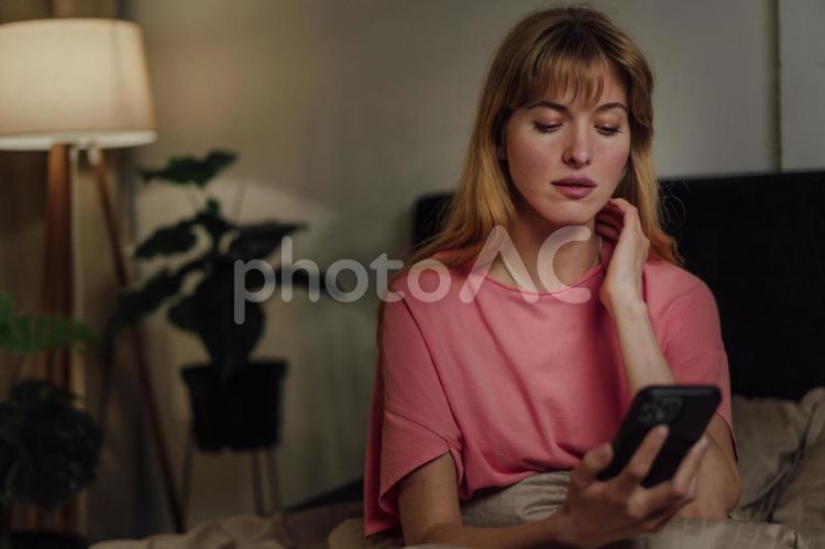 ベッドでスマートフォンを使っている女性 女性,外国人,欧米人の写真素材