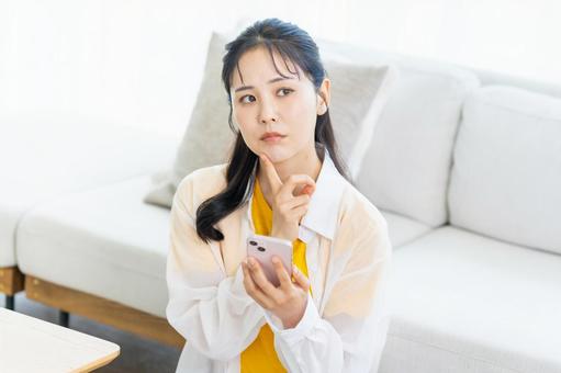 スマホを持って考える若い女性 スマホ,困る,悩むの写真素材