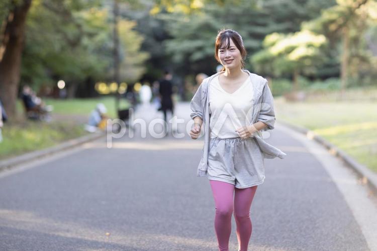 カメラ目線で道路をジョギングする女性（全身） 女性,ジョギング,走るの写真素材