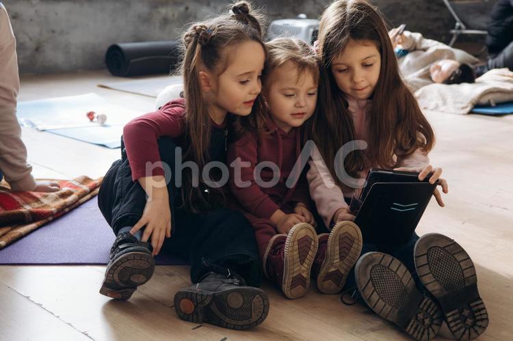 みんなでタブレットを見る女の子と後ろで寝転ぶ女性 女性,女の子,人物の写真素材