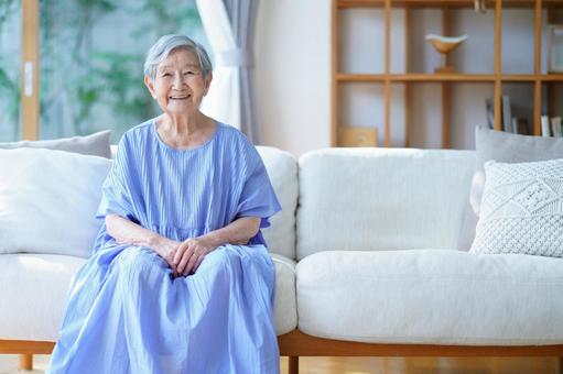 にっこり笑う青いワンピースのおばあちゃん 女性,ソファ,座るの写真素材