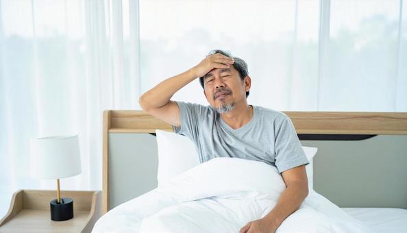 寝起きで座って頭を抱えるパジャマ姿の男性 寝起きで座って頭を抱えるパジャマ姿の男性の写真