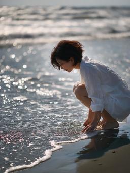 光が差し込むビーチ:水面に触れる若い女性 光が差し込むビーチ:水面に触れる若い女性の写真
