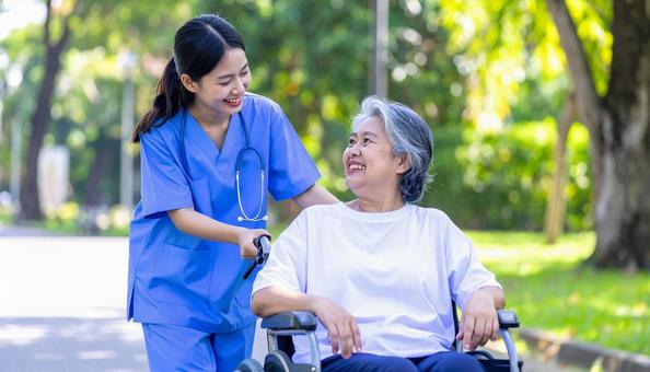 散歩する車椅子の高齢女性と女性介護士 散歩する車椅子の高齢女性と女性介護士の写真