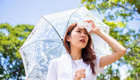 日傘をさして白いハンカチで汗を拭く女性 日傘をさして白いハンカチで汗を拭く女性の写真