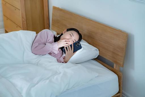 あくびをして携帯を見る女性 あくびをして携帯を見る女性 携帯電話,トラブル,夜更しの写真素材