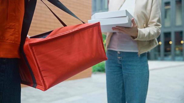 屋外でピザのデリバリーを受け取る女性と保温バッグを持つ配達員の男性 配達,フードデリバリー,デリバリーの写真素材