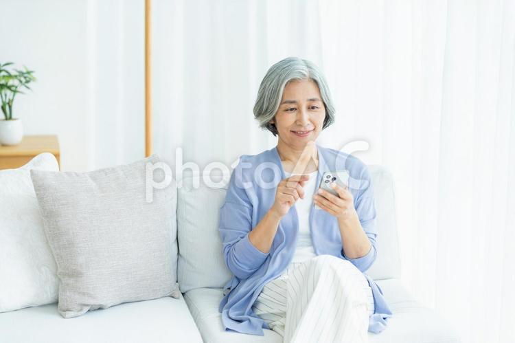 リビングでスマホを操作するシニア女性 シニア,スマホ,笑顔の写真素材