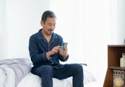 寝室でスマホを見るミドルの男性 男性,スマホ,ミドルの写真素材