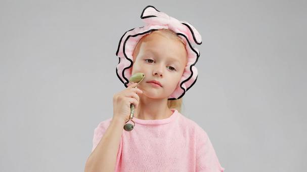 疲れた顔でフェイスローラーをする女の子 疲れた顔でフェイスローラーをする女の子の写真