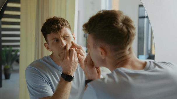 鏡で頬を見ている男性 鏡,映る,顔の写真素材