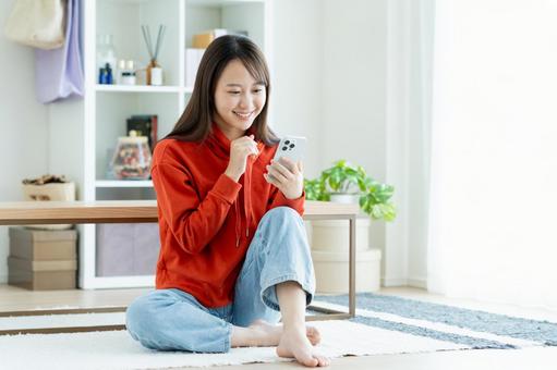 リビングでスマホを見る若い女性 女性,笑顔,家の写真素材