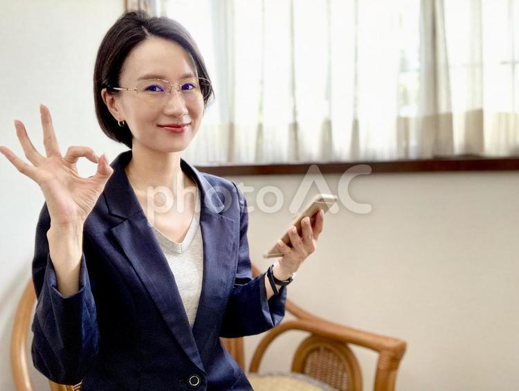 スマホを持ちながらOKサインを出す女性 女性,スーツ,スマホの写真素材