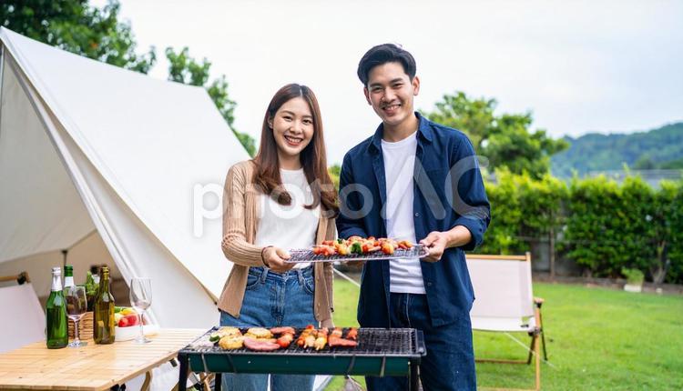 バーベキューで串を持って笑顔の男女 バーベキュー,キャンプ,アウトドアの写真素材