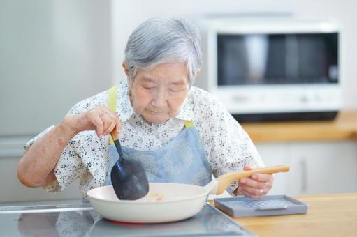 調理器具を持ちフライパンを見つめる女性 女性,料理,フライパンの写真素材