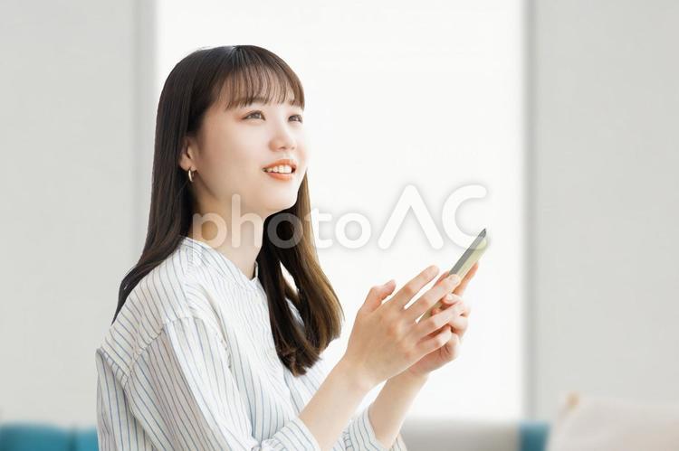リビングでスマホを持つ笑顔の女性 リビングでスマホを持つ笑顔の女性 女性,スマホ,スマートフォンの写真素材