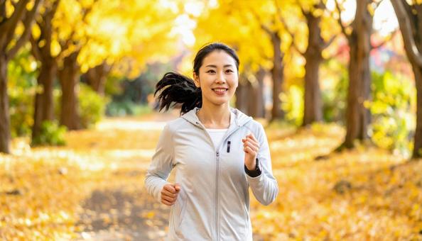紅葉の中でジョギングをする若い日本人女性 紅葉の中でジョギングをする若い日本人女性の写真