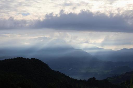 雲の多い空と薄明光線と幻想的な山並みの写真