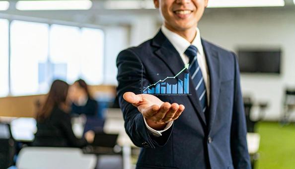 右上がりのグラフを片手に持つビジネスマンの写真