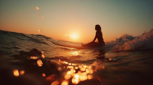 夕暮れの海で最後の波に乗るサーファー女性 夕暮れの海で最後の波に乗るサーファー女性の写真