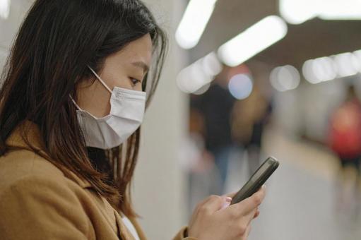駅のホームで電車を待つマスク姿の女性 駅のホームで電車を待つマスク姿の女性の写真