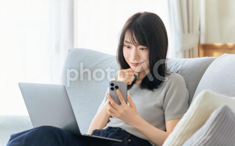 ソファに座ってスマホとパソコンを使う女性 女性,ソファ,パソコンの写真素材