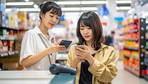 スーパーでスマホ決済を使う若い日本人女性 スーパーでスマホ決済を使う若い日本人女性の写真