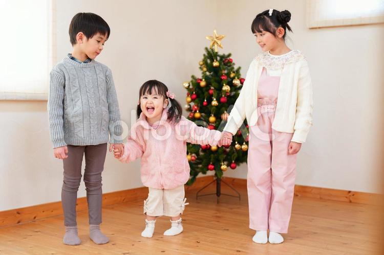 ご機嫌な女の子とツリーの前で手を繋いでいる子供たち 男女,手を繋ぐ,仲良しの写真素材