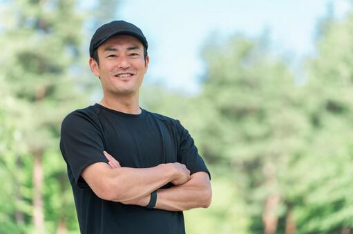 新緑の公園で腕組みをするアジア人男性 スポーツ,スポーツウェア,腕組みの写真素材