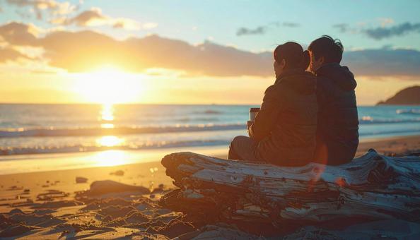 ビーチで沈む夕日を眺めるカップル ビーチで沈む夕日を眺めるカップルの写真