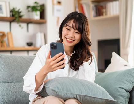 自宅のリビングでスマホを操作する女性 自宅のリビングでスマホを操作する女性の写真