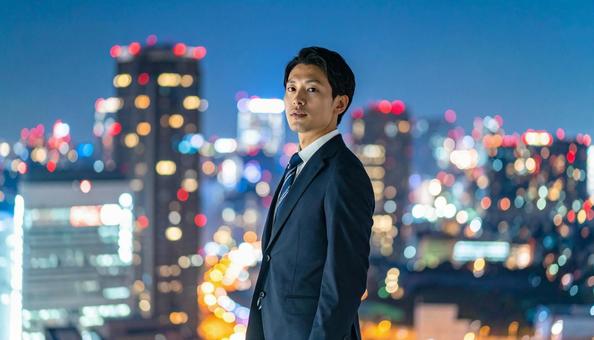 都市の夜景を背景に佇むビジネスマン 都市の夜景を背景に佇むビジネスマンの写真