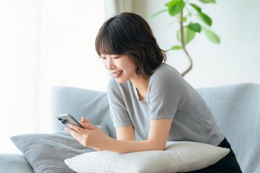 ソファに座ってスマホを使う笑顔の女性 ソファに座ってスマホを使う笑顔の女性の写真