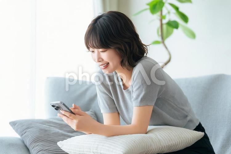 ソファに座ってスマホを使う笑顔の女性 女性,スマホ,スマートフォンの写真素材