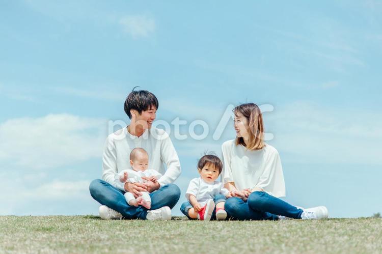 空と芝生に座る家族・ファミリー（4人） 家族,親子,赤ちゃんの写真素材