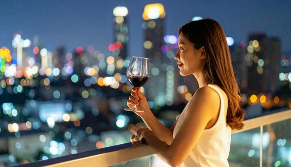 夜景を背景にバルコニーでワインを持つ女性 夜景を背景にバルコニーでワインを持つ女性の写真