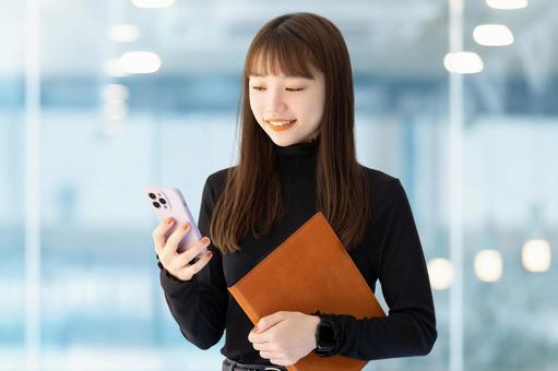 スマホとバインダーを持つ笑顔の女性 スマホとバインダーを持つ笑顔の女性 女性,スマホ,笑顔の写真素材