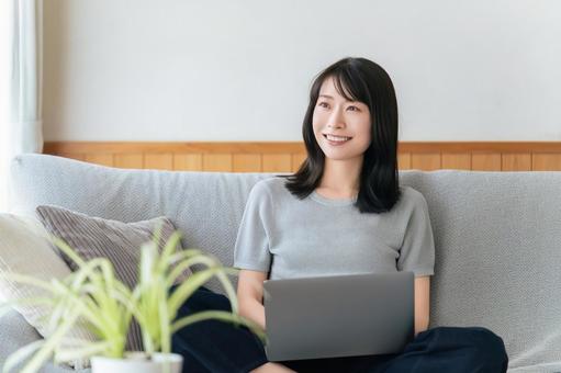 ソファに座ってパソコンを使う女性 ソファに座ってパソコンを使う女性の写真