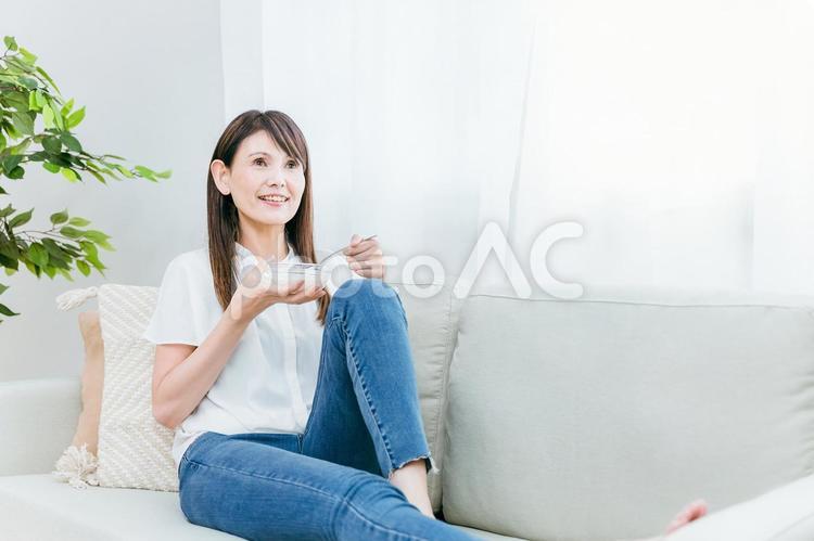 ソファでヨーグルトを食べる女性（笑顔） ヨーグルト,乳酸菌,菌活の写真素材