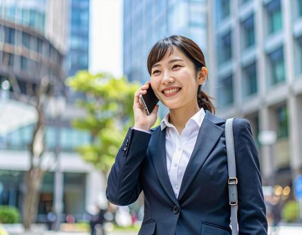 街中で電話をかける若い女性社員 街中で電話をかける若い女性社員の写真