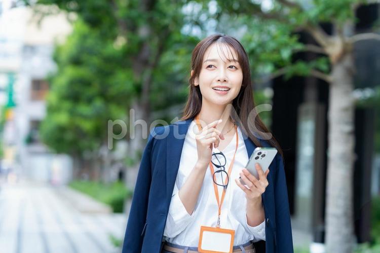 ビジネス街を歩くビジネスウーマン スマホ,ビジネスウーマン,笑顔の写真素材