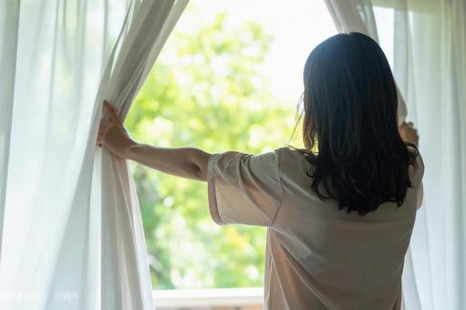 白いレースのカーテンを開く女性 白いレースのカーテンを開く女性の写真