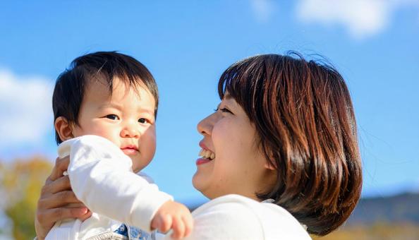 青空の下、子供を抱っこする母親 青空の下、子供を抱っこする母親の写真